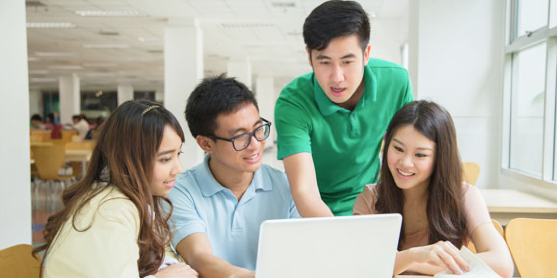 Students collaborating around a laptop in a bright study area